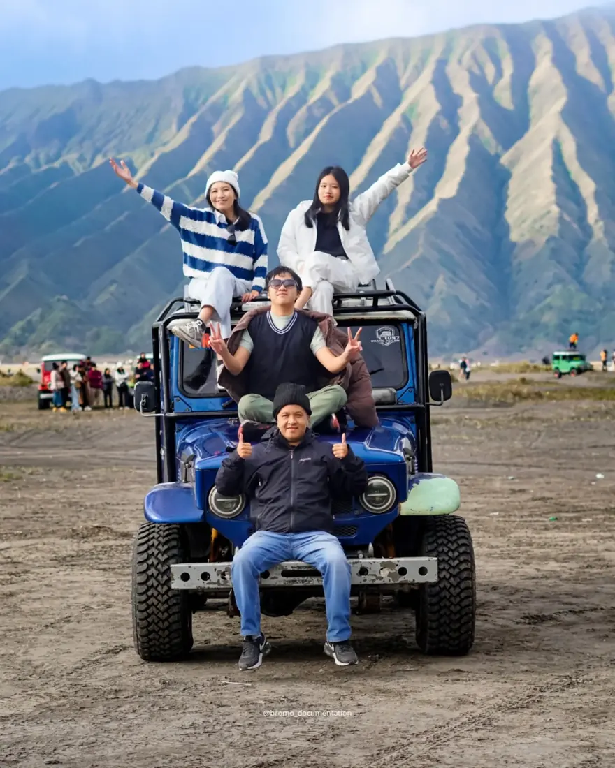 Rombongan tamu di atas jeep biru dengan latar bukit Bromo