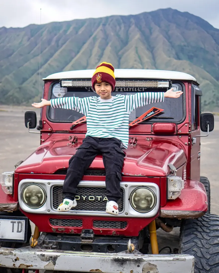 Anak kecil berpose di kap jeep merah