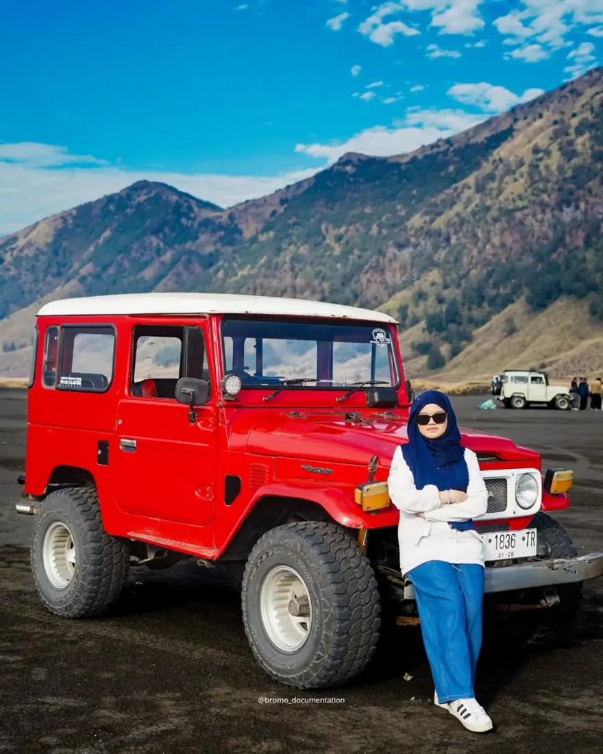 Tamu berpose di samping jeep merah di lautan pasir